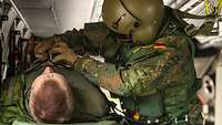 Ein Soldat mit Fliegerhelm betreut in einem Hubschrauber einen liegenden Patienten.