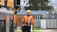 Ein Mann mit Schutzhelm und orangener Warnweste steht neben einem gelben Fahrzeug