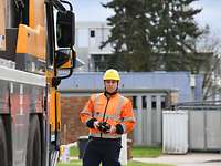 Ein Mann mit Schutzhelm und orangener Warnweste steht neben einem gelben Fahrzeug