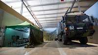 Ein LKw steht in einer Halle mit Tarnnetzen und einem Zelt