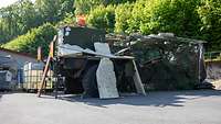 Ein Bundeswehrfahrzeug unter einem Tarnnetz und Gerümpel
