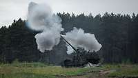 Eine Panzerhaubitze 2000 schießt im Gelände. Rauch liegt in der Luft.