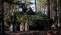 GTK Boxer bei der Übung Mighty Arrow in Finnland Ein mit Zweigen getarnter GTK Boxer steht im Wald. Ein Soldat schaut aus der Luke.