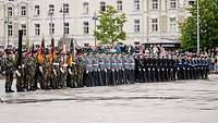 Soldaten mit Fahnen und in verschiedenen Uniformen stehen mit geschulterten Waffen in Formation.