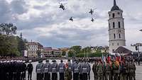 Hubschrauber fliegen über dem Appellplatz mit Soldaten in Formation.