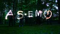 Menschen schreiben mit Licht „ASEM“ in die Luft