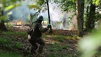 Vorbereitung zum Nebeln im Gelände Ein Soldat wirft einen Nebelkörper im Wald, im Hintergrund brennt es an einigen Stellen.