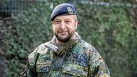 Ein Soldat in Flecktarn blickt zum Porträt in die Kamera, hinter ihm sind Tarnnetze eines SDP zu sehen.