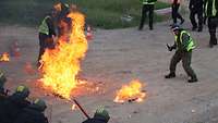 Ein Darsteller in grellgelber Warnweste steht vor einem Feuerball.