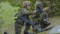 Zwei Soldaten knien nebeneinander und zeigen in die gleiche Richtung.
