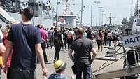Spectators watch a low-flying helicopter above the harbour, with grey ships in the background