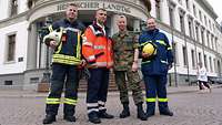 Four men in different uniforms standing in front of the parliament building of Hesse