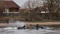 Ein Transportpanzer fährt durch einen breiten Fluss.