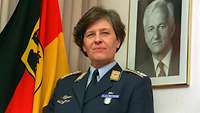 Dr. Verena von Weymarn Eine Soldatin im Porträt sitzend vor einer Truppenfahne und einem Bild von Richard von Weizsäcker