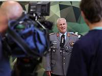 Ein Mann in Uniform steht vor einem Mikrofon und einer Fernsehkamera
