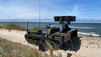 Ein Kettenpanzer der Bundeswehr mit einer Raketenabschussvorrichtung steht in den Dünen vorm Meer.
