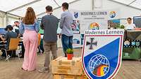 Modernes Lernen am MINT-Campus Im Vordergrund steht ein Schild, dahinter drei Jugendliche, die auf einen Bildschirm gucken.