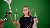 Ein Mädchen hält in der linken Hand eine Flasche und in der rechten eine Spritze, welche mit einem roten Schlauch verbunden ist