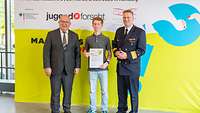 Gewinner des Sonderpreises Drei Männer stehen vor einem gelben Plakat