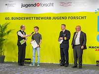 Als Erster auf dem Podium - Siegerpreisverleihung Vier Männer stehen auf einer Bühne mit einem gelben Hintergrund