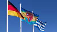 Eine Deutschland-, eine Griechenland- und eine Einheitsfahne wehen an Fahnenmasten im Wind.