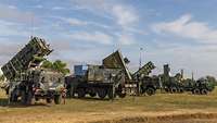 Mehrere militärische Fahrzeuge der NATO-Flugabwehr sind auf einer Wiese ausgestellt.