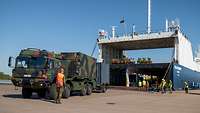 Ein militärischer LKW steht vor der offenen Ladefläche einer großen Fähre.