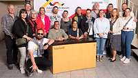 Menschen stehen vor einer bedruckten Leinwand und schauen in die Kamera