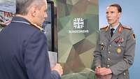 „Nachgefragt“ mit Generalmajor Dr. Christian Freuding Zwei Soldaten stehen sich gegenüber vor einem Monitor und sprechen miteinander