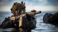 Ein Soldat steht mit dem Gewehr G95 im Anschlag im Wasser