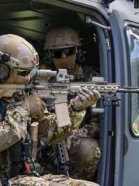 Ein Soldat sitzt mit dem Gewehr G95 im Anschlag im Hubschrauber