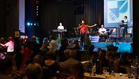 Eine Band spielt auf einer Bühne und davor tanzen Menschen.
