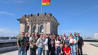 Menschen stehen auf dem Dach des Reichstages, Im Hintergrund ein Turm mit der deutschen Flagge.