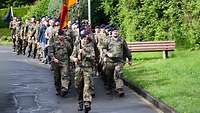 Soldaten und vereinzelt Zivilisten marschieren, im Vordergrund eine Bundesdienstflagge