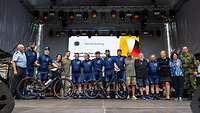 Eine Gruppe Fahradfahrende stehen auf einer Bühne