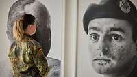 Eine Soldatin steht vor einem Portrait eines Soldaten in einer Ausstellung