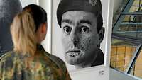 Eine Soldatin steht vor einem Scharz-Weiß-Portrait eines Soldaten in einer Ausstellung