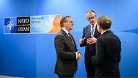 NATO-Gipfel 2025 Boris Pistorius und Friedrich Merz stehen zusammen und unterhalten sich, im Hintergrund das NATO-Logo