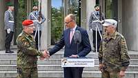 Friedrich Merz steht hinter einem Rednerpult und schüttelt einem Soldaten die Hand