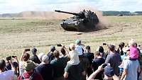Menschen mit Handys in der Hand beobachten eine fahrende Panzerhaubitze 2000