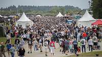 Viele Menschen bewegen sich auf einem Gelände mit ausgestellten Militärfahrzeugen und Infoständen