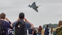 Menschen beobachten ein Kampfflugzeug vom Typ Eurofighter mit Nachtbrenner im Flug am Himmel