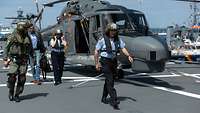 Drei Soldaten und ein Mann gehen vor einem stehenden Hubschrauber vom Typ Sea Lynx entlang