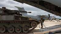 Schützenpanzer trifft auf Flugzeug Ein Panzer und ein Soldat stehen an der Heckrampe eines großen Flugzeugs auf dem Flugplatz.