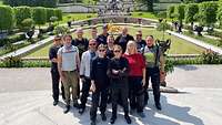 Menschen stehen vor einem Schlossgarten und blicken in die Kamera