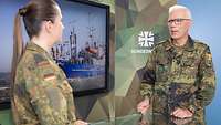 Eine Soldatin und ein Soldat stehen sich vor einem Monitor gegenüber und sprechen miteinander