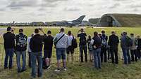 Menschen stehen hinter Absperrzäunen und beobachten ein Kampfflugzeug Tornado vor einem Hangar stehend