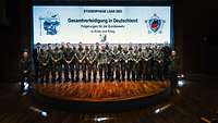 Die Lehrgangsteilnehmenden stehen mit dem Generalinspekteur auf der Bühne für ein Gruppenfoto. 