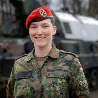 Eine Soldatin blickt freundlich in die Kamera. Im Hintergrund steht eine Panzerhaubitze.