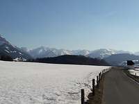 Landstrasse mit Blick auf schneebedeckte Wiesen und Berge